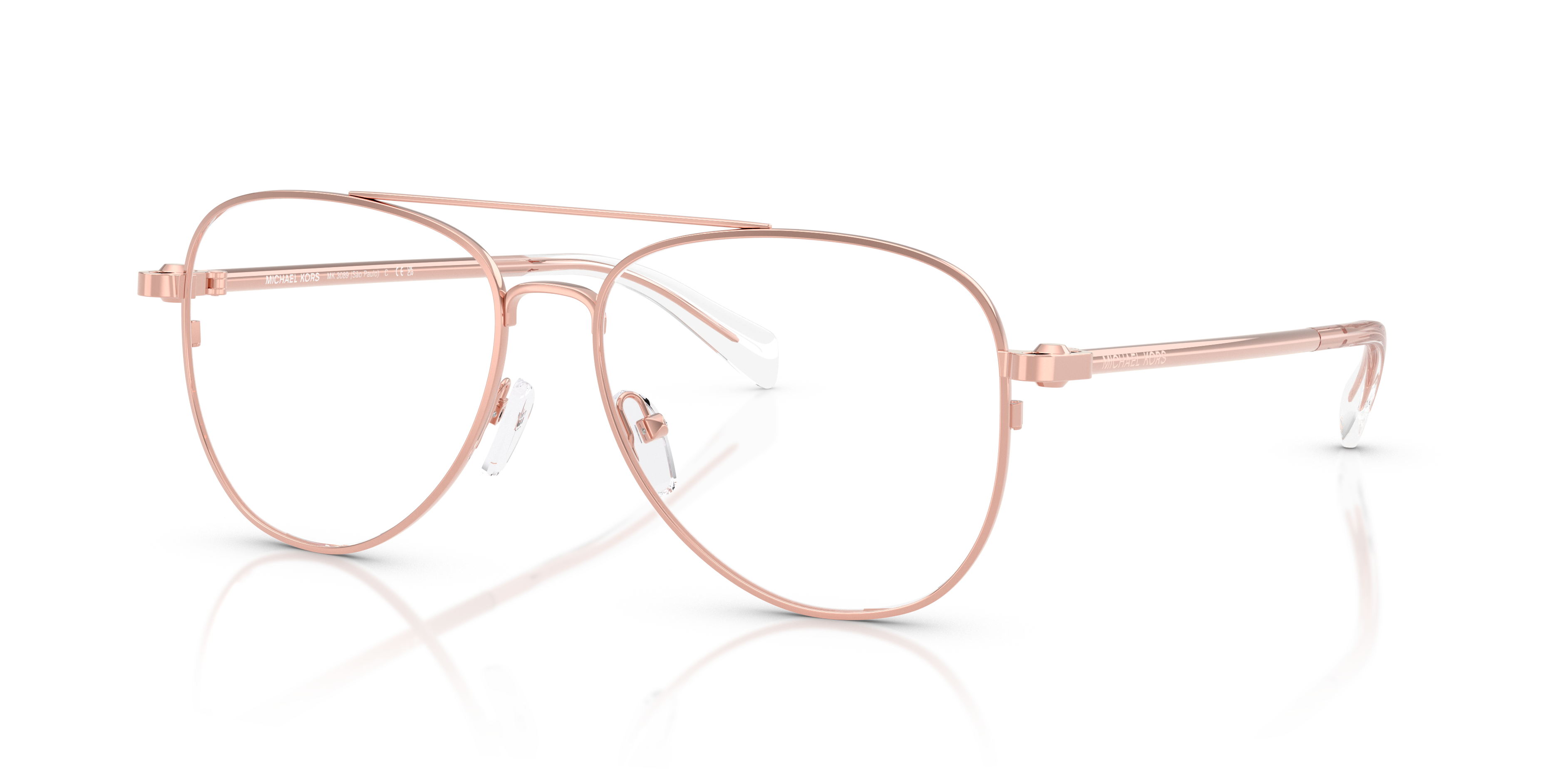 Donna sorridente che indossa occhiali da sole Michael Kors 0MK3089 Rose Gold Shiny, che riflettono un paesaggio urbano.