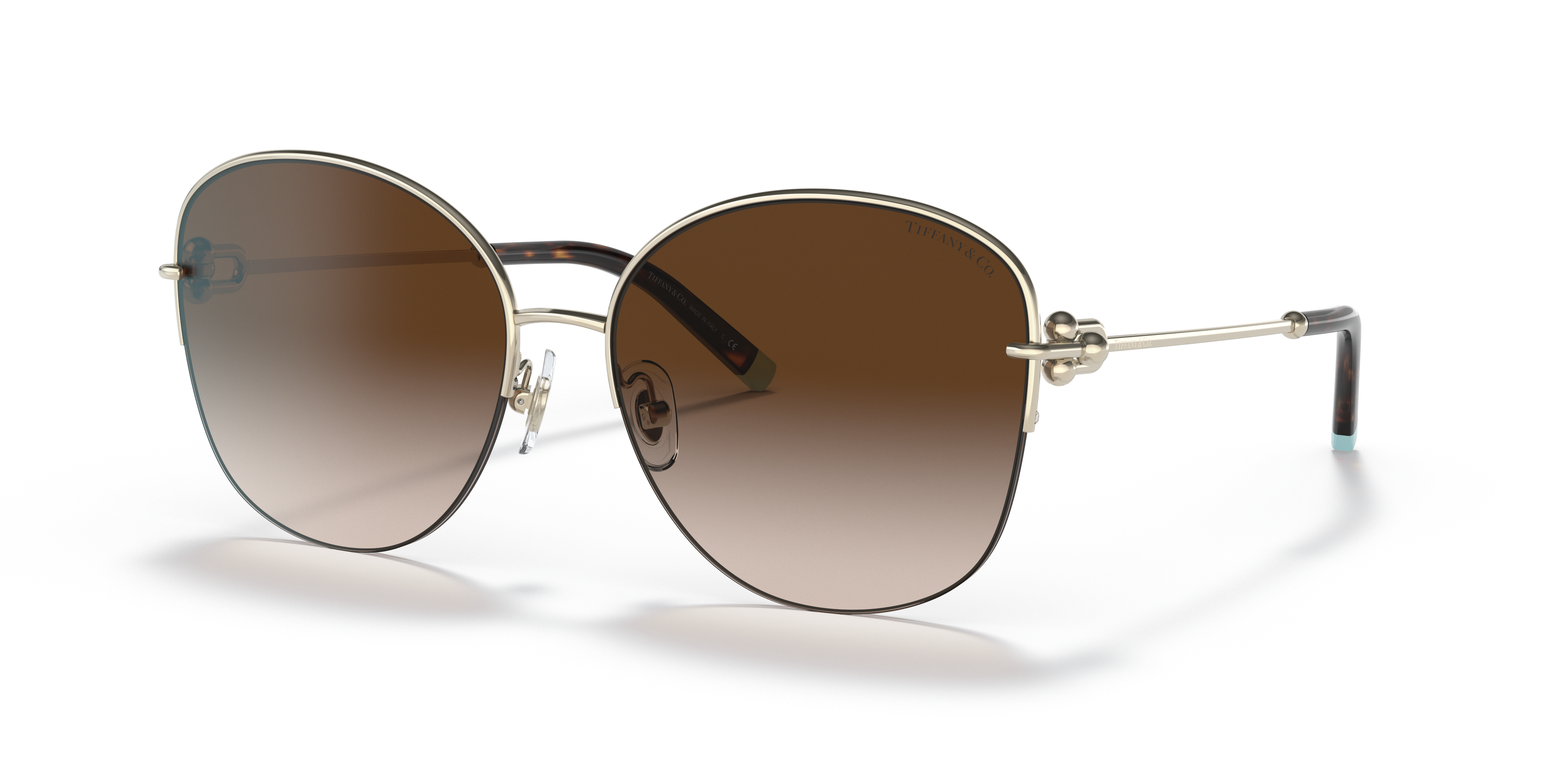Occhiali da sole Tiffany TF3082 da donna color oro pallido con lenti marroni sfumate, posati su una superficie chiara