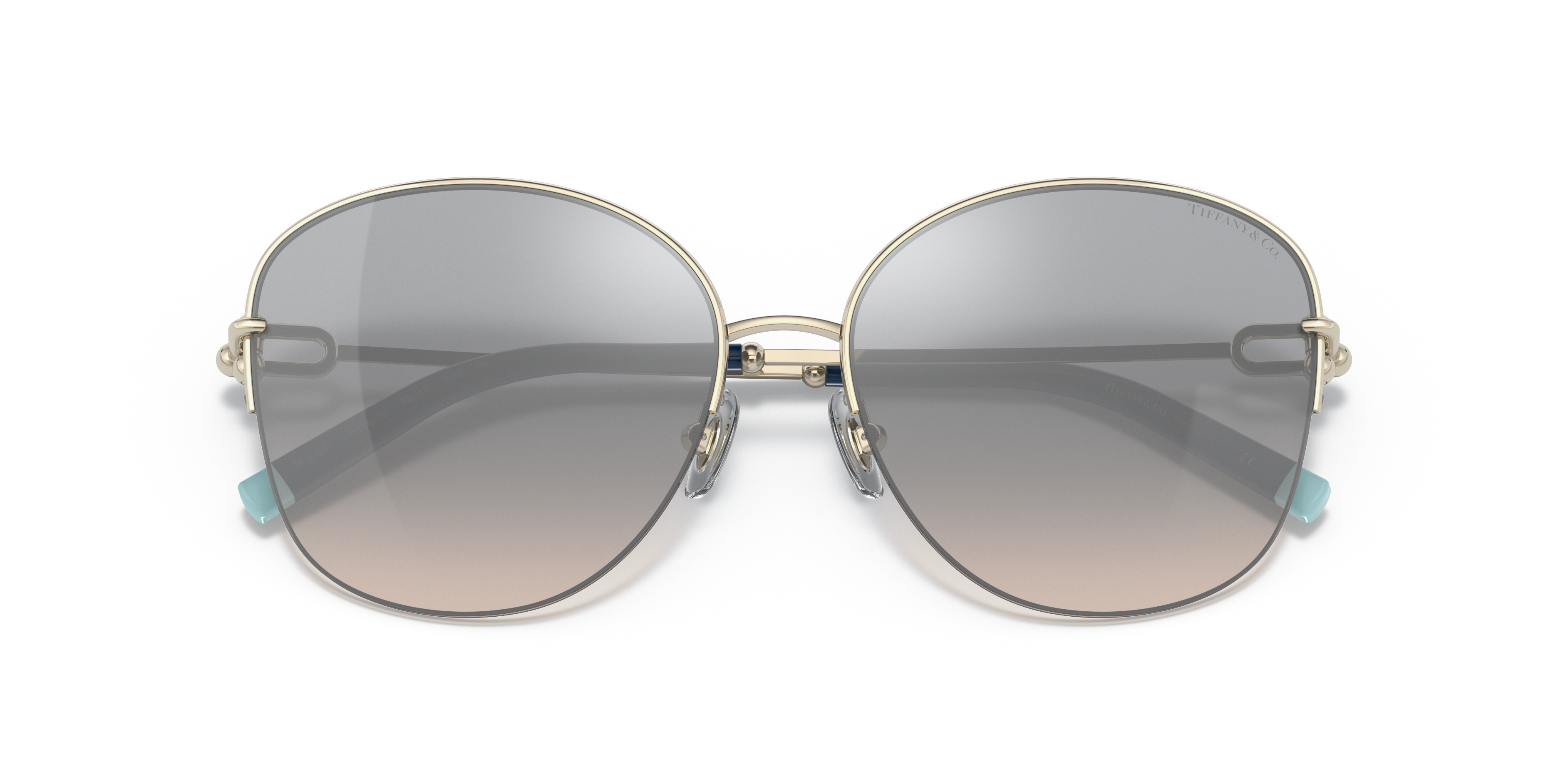 Occhiali da sole Tiffany TF3082 da donna color oro pallido con lenti marroni sfumate, posati su una superficie chiara